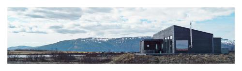 a glass building with mountains in the background at Austurey - Lakefront Villa in Laugarvatn