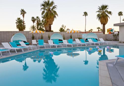 a pool at a resort with blue chairs and palm trees at The Cole in Palm Springs