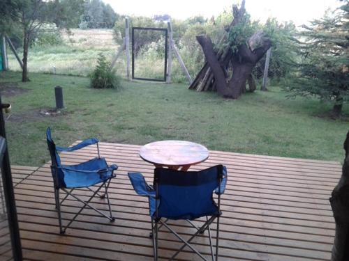 two chairs and a table on a wooden deck at Cabañas Orillas del Chimehuín in Junín de los Andes