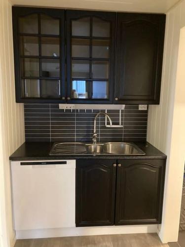 a kitchen with black cabinets and a sink at Flott leilighet sentralt på Tromsøya in Tromsø