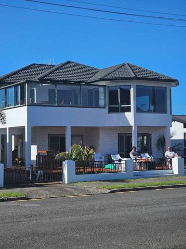 a large white house with people sitting at tables in front of it at Whangamata Harbour Haven in Whangamata
