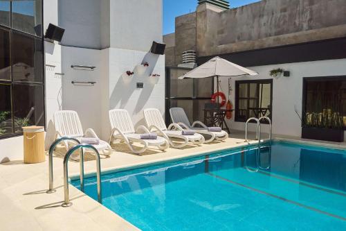 a swimming pool with white chairs and an umbrella at Ramada by Wyndham Buenos Aires Centro in Buenos Aires