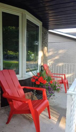 two red chairs sitting on a porch with flowers at Birdsong Bungalow in Port Dover