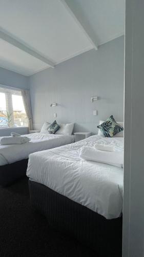 two beds in a hotel room with white sheets at The Tree Motel in Narooma