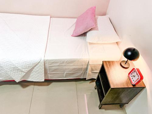a bed with white sheets and a clock on a table at Apto cerca Estadio Metropolitano in Barranquilla