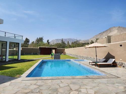 a swimming pool with an umbrella next to a house at Casa de campo de estreno en Cieneguilla, Lima-Perú in Cieneguilla