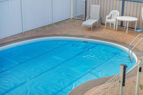 a large blue swimming pool with two chairs and a table at Harbour Lights - townside with a pool in Merimbula