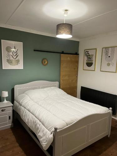 une chambre avec un lit blanc et un mur vert dans l'établissement Petite maison de village, à Saint-Jean-sur-Mayenne