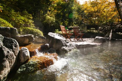 two chairs sitting next to a river with rocks at Saito Hotel in Ueda