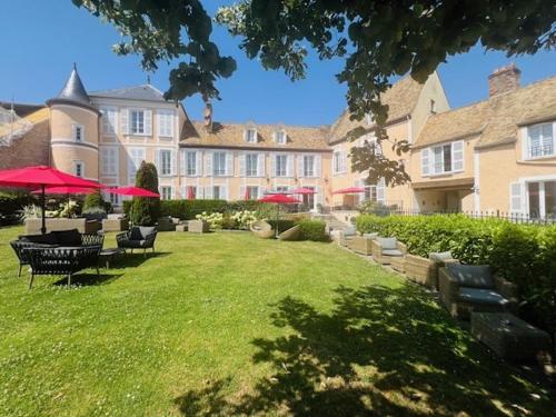 a large building with chairs and umbrellas in a yard at Hôtel Saint-Laurent, The Originals Relais in Montfort-lʼAmaury