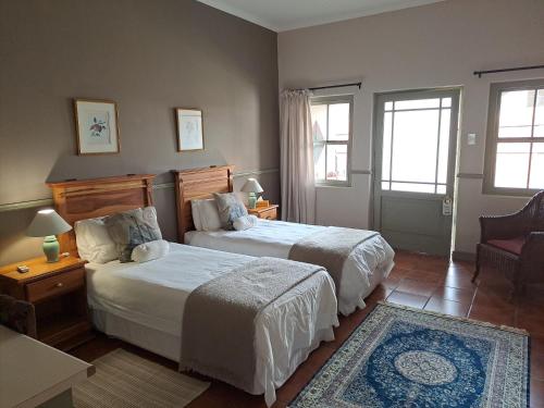 a bedroom with two beds and a chair and two windows at HouseMartin Lodge & Self Catering in De Rust