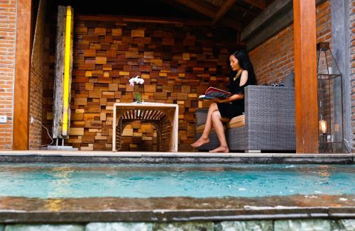 a woman sitting on a bench reading a book next to a fireplace at Kaleydo Villas in Gili Trawangan