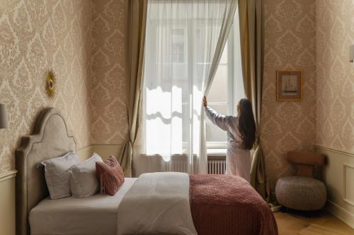 a woman is looking out the window of a bedroom at Hotel Unicus Palace Old Town - Destigo Hotels in Kraków