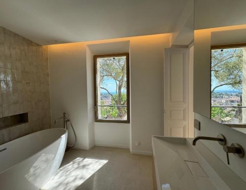 - une grande salle de bains blanche avec baignoire et 2 fenêtres dans l'établissement Luxueuse villa Mougins, à Mougins
