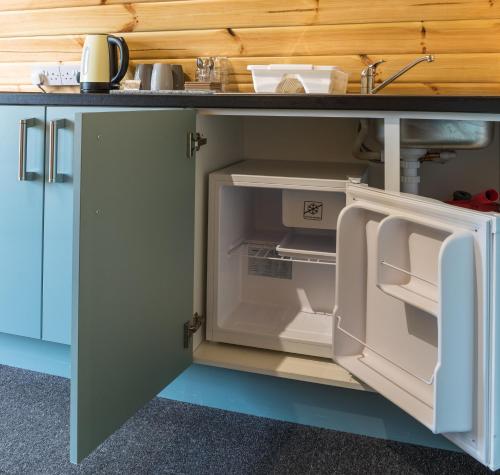 an open refrigerator in a kitchen under a counter at Cosy Glamping In the Eskdale Valley - Studio Lodges and Mega Pods in Eskdale