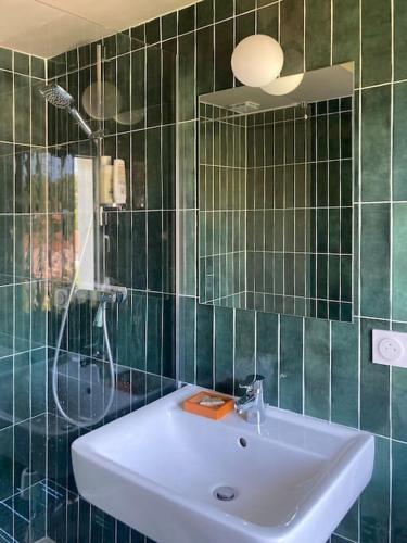 La salle de bains est pourvue de carrelage vert, d'un lavabo et d'une douche. dans l'établissement Appartement au cœur du village - Les Fougères Tardets, à Tardets-Sorholus