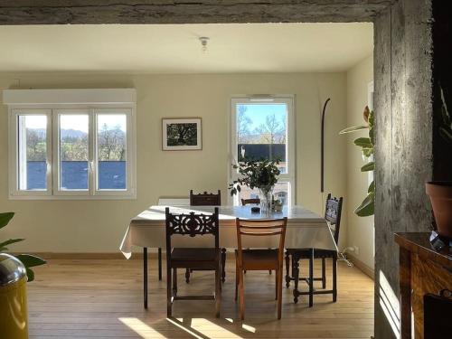 una sala da pranzo con tavolo e sedie e due finestre di Appartement au cœur du village - Les Fougères Tardets a Tardets-Sorholus