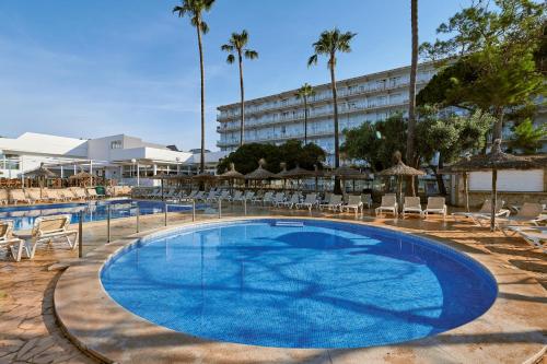 Una gran piscina con sillas y un hotel. en AluaSun Cala Antena - All Inclusive, en Calas de Mallorca