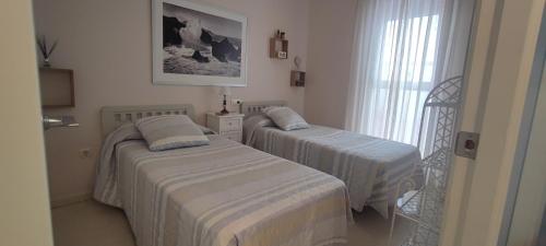 two beds in a small room with a window at Apartamento la paz. Un lugar para descansar. in Isla Cristina