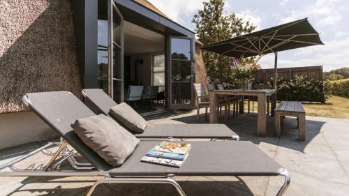 a patio with two chairs and a table and an umbrella at Dutchen Park Weideduyn in Schoorl