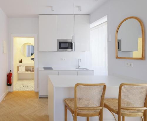 eine weiße Küche mit Stühlen und eine Kücheninsel in der Unterkunft Apartamentos La Colonia de Muros in Muros de Nalón