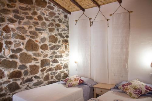 a room with two beds and a stone wall at Domo Bangone - Sa Corte in Orosei