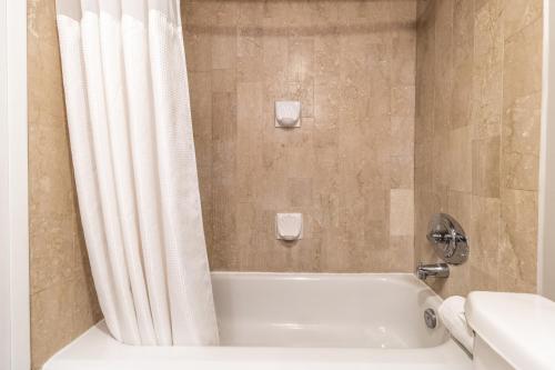 a bathroom with a tub and a shower curtain at Atrium Hotel Vancouver in Vancouver