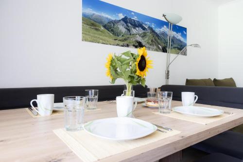 a wooden table with plates and a vase with a sunflower at Appartement Schareckblick in Bad Gastein