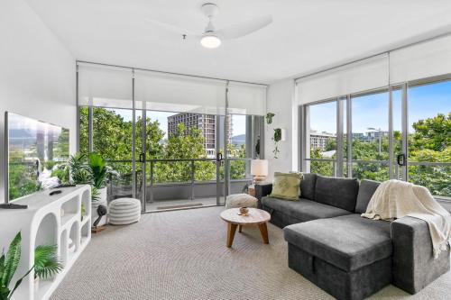 a living room with a gray couch and large windows at Coastal Harbour Lights I Pool, Gym & prime Location in Cairns