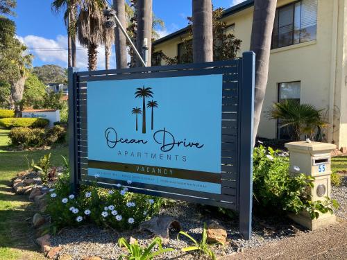 a sign in front of a house with palm trees at Ocean Drive Apartments in Merimbula
