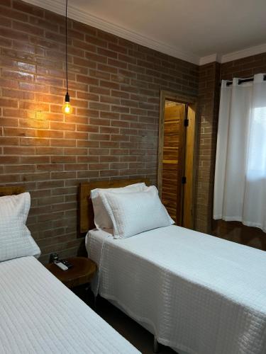 a bedroom with two beds and a brick wall at Pousada Bem Viver in Nobres