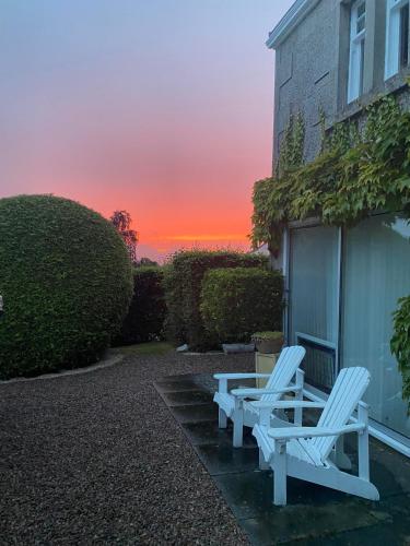 two white chairs sitting outside of a house with a sunset at Glenburn, Fochabers in Fochabers