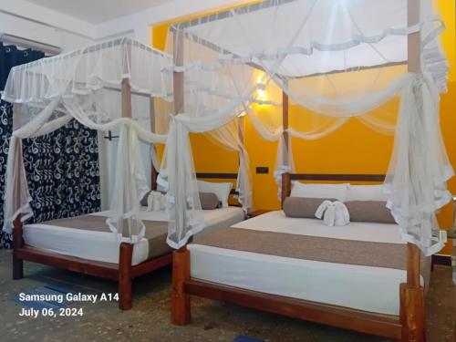two beds with white drapes in a bedroom at Peacock Riverside in Udawalawe
