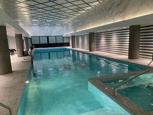 a large swimming pool with blue water in a building at Amazing 1 Bedroom Apt with Large living & extra sleeping space -up to 5 ppl Plus Gym Jacuzzi Spa Pool Sauna and Garden with BBQ in Sydney