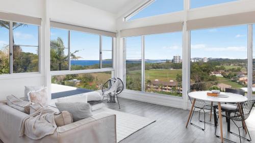 a living room with a couch and a table and windows at The Lookout Lounge - Pet Friendly, Pool, Great Views! in Coffs Harbour