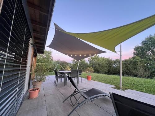 un patio avec une table, des chaises et un parasol dans l'établissement L écrin verdoyant, à Jonzier-Épagny