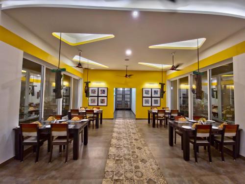 a dining room with tables and chairs and yellow walls at Tathastu Tadoba in Mohurli