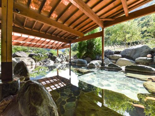 a patio with a pond with rocks and a wooden roof at Iwazonokan in Minami Alps