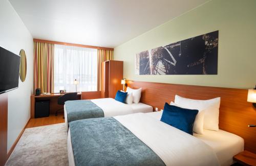 a hotel room with two beds and a desk at Leonardo Hotel Salzburg Airport in Salzburg