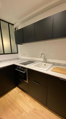 - une cuisine avec des placards noirs, un évier et une cuisinière dans l'établissement Joli studio au cœur de Paris, à Paris