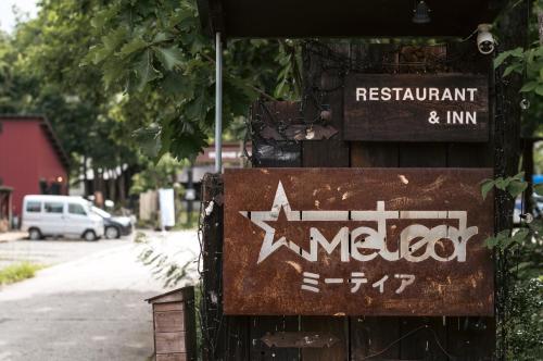 a sign for a restaurant and inn on the side of a street at Hakuba Pension & Log Hotel Meteor in Hakuba