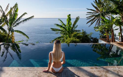 a woman sitting on the edge of a pool looking out at the ocean at Pirate House Sea front Private Pool Garden Funchal in Funchal