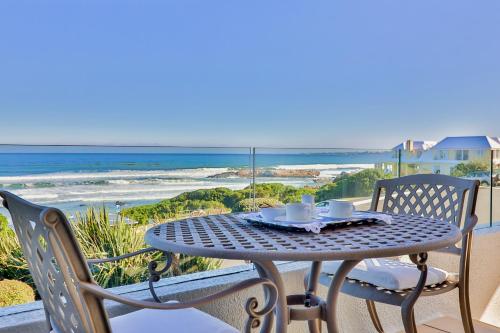 a table with two cups and plates on a balcony with the beach at Hermanus Beachfront Lodge - Solar Power in Hermanus