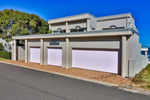 a white garage with two gates on a street at Hermanus Beachfront Lodge - Solar Power in Hermanus