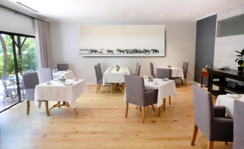 una sala da pranzo con tavoli e sedie bianchi e un pianoforte di Vine Guesthouse a Stellenbosch