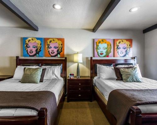 two beds in a room with paintings on the wall at Rodeway Inn & Suites Williams Downtowner-Rte 66 in Williams