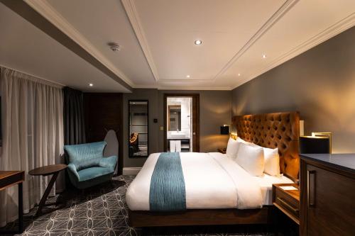 a hotel room with a bed and a blue chair at 100 Queen's Gate Hotel London Kensington, Curio Collection by Hilton in London