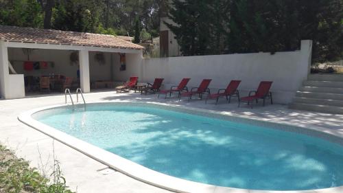 - une piscine avec des chaises rouges et un mur blanc dans l'établissement Studio en Provence, à Mimet
