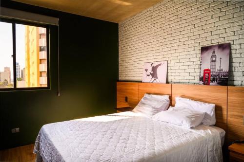 a bedroom with a white bed with a brick wall at Luix Londrina Flat Hotel , 707, QS completo in Londrina