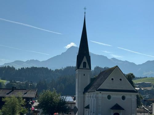 a church with a steeple with a mountain in the background at CHALET KITZBICHL by Alpin Charme Apartments in Reith bei Kitzbühel
